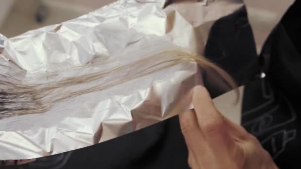 Detailní záběr procesu zvýraznění dlouhé hnědé vlasy dívky. Kadeřník připravuje silné krásné vlasy dívky pro zvýraznění, česání vlasů, balení mokré vlasy do fólie — Stock video