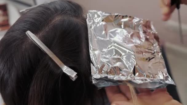 Close-up of the process of highlighting the long brown hair of a girl. The hairdresser prepares the strong beautiful hair of the girl for highlighting, combing the hair, wrapping wet hair in foil — Stock Video