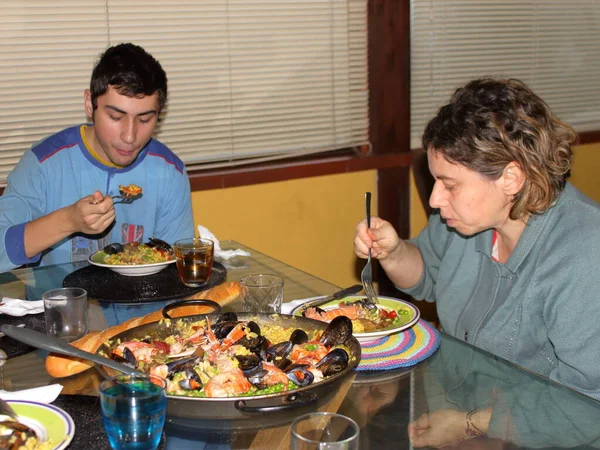 Matka a syn sedí u stolu a jedí tradiční španělskou paellu — Stock fotografie