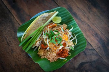 Tayland usulü kızarmış erişte, popüler sokak yemekleri, yeşil muz yaprağıyla lezzetli Tayland mutfağı, eski ahşap masa üzerinde düz görünüm konseptiyle ünlü..