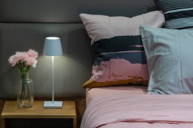 Konforlu yatak odasındaki modern yatak odası lambası. Cam bir şişede pembe karanfiller, modern kumaş yastıklar. İç dekorasyon, oturma odası dekorasyonu.