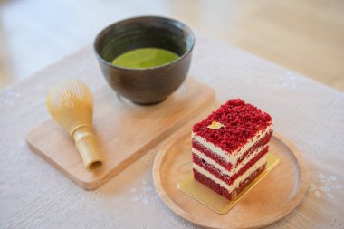 Kırmızı kadife kek suratı tereyağı ve yumuşak krema ile ahşap tahta üzerine kesilmiş yumuşak odaklı Japon yeşil çay eşleşmesi arka planında. Bir dilim kek. Ahududulu kek. Lezzetli tatlı. Geleneksel Amerikan tatlı konsepti.