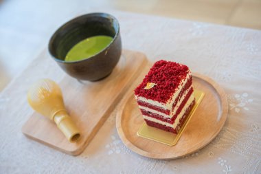 Kırmızı kadife kek suratı tereyağı ve yumuşak krema ile ahşap tahta üzerine kesilmiş yumuşak odaklı Japon yeşil çay eşleşmesi arka planında. Bir dilim kek. Ahududulu kek. Lezzetli tatlı. Geleneksel Amerikan tatlı konsepti.