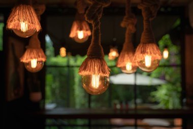 Klasik tavan avizesi kenevir ipinden gelen parlak ampuller pembe neon kelebek iç kısmı, yuvarlak pencere ve yeşil doğa arka planı. Dekorasyon retro ev, restoran kavramları.