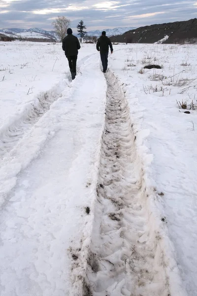 A deep footprint on the road from a car wheels in the snow. Silhouettes of people walking away along the road.