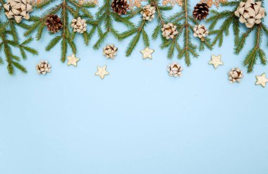 Yeşil Noel ağacı dalları ve yeni yıl oyuncakları. Gökyüzü mavisi arka planda koniler, yaylar ve altın yıldızlar. Metin için boşluk
