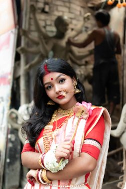 Durga Idol 'un önünde duran güzel Hintli kızın portresi. Geleneksel Hint sarisi, altın mücevher ve bilezik takıyor. Maa Durga agomoni çekim konsepti.