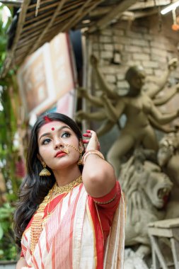 Durga Idol 'un önünde duran güzel Hintli kızın portresi. Geleneksel Hint sarisi, altın mücevher ve bilezik takıyor. Maa Durga agomoni çekim konsepti.