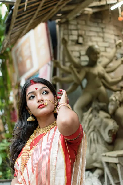 Durga Idol 'un önünde duran güzel Hintli kızın portresi. Geleneksel Hint sarisi, altın mücevher ve bilezik takıyor. Maa Durga agomoni çekim konsepti.