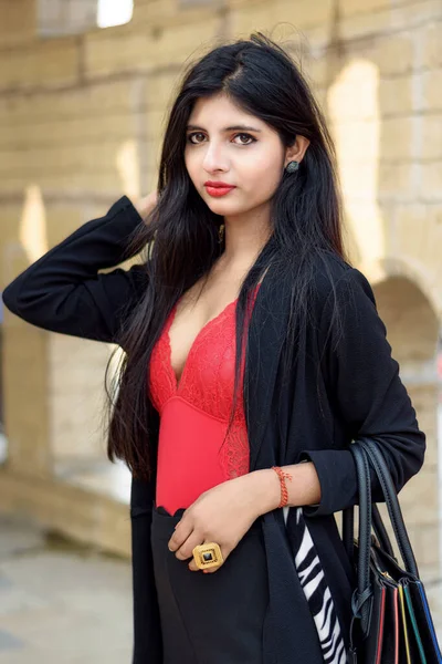 形象非常漂亮的年轻迷人的印度女人穿着红色衣服 黑色夹克 拿着黑色大手提包 在模糊的背景下摆出时髦的样子 生活方式和时尚 — 图库照片