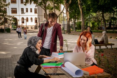 Genç öğrenciler birlikte çalışır, sohbet eder, bilgisayara bakar, film izler ve okulun bahçesinde gülerler. Üniversite, kampüs, okul bahçesi, Müslüman öğrenci, Hıristiyan, Yahudi, farklı insanlar.