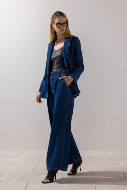 Büyük beden kot pantolon ve deri bluz giyen modaya uygun moda bir kadın, beyaz arka planlı minimalist stüdyoda güven içinde poz veriyor. Modern yaşam tarzı, moda eğilimleri ve kopyalama alanı.