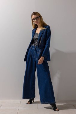 Şık, modern bir kadın, büyük beden kot ceket ve deri bluzlu geniş bacak pantolonu giyiyor. Minimalist stüdyoda güvenle poz veriyor. Moda, yaşam tarzı, fotokopi alanı ile iş gündelik konsepti.