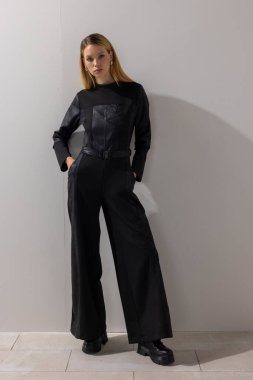 Zarif siyah tulum giyen, minimalist stüdyoda beyaz duvara karşı poz veren kendinden emin modern bir kadın. Çağdaş moda, iş tarzı, yaşam tarzı konsepti ve kopyalama alanı.