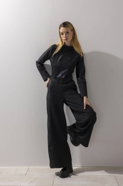 Modern, kendine güvenen, şık siyah tulum giyen, minimalist stüdyoda beyaz duvara karşı güçlü duruşuyla poz veren bir kadın. Güç modası, yaşam tarzı, liderlik ve kopyalama alanı.