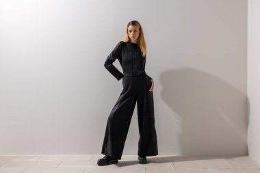 Modern siyah tulum giyen, geniş kopya alanı olan minimalist stüdyoda poz veren kendine güvenen bir kadın. Güç sargısı, çağdaş moda, yaşam tarzı ve editoryal konsept.