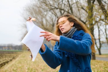 Mavi paltolu güzel bir kadın açık rüzgarlı bir alanda kalır ve yanan kağıt çarşafı alevler içinde yakar.