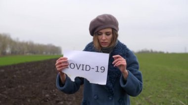 Kadın elinde yazılı Covid-19 sözcüğüyle kağıt tutuyor.