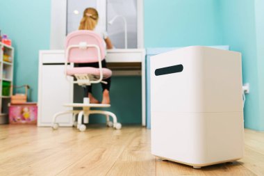 Arka planda çocuk otururken odada büyük kare beyaz nemlendirici kutusu var. Kendini soyutlama sırasında rahat bir ev konaklaması.