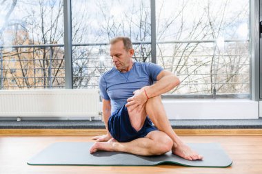 Orta yaşlı sporcu, spor yaparken hafif stüdyoda paspasın üstünde kıvrılır ve vücut kaslarını gerer.