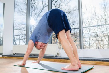 Middle yaşını dolduran adam yerde kalır, yoga eğitimi alır, köpek pozu verir, hafif fitness stüdyosunda vücut kaslarını düzenler ve büker.