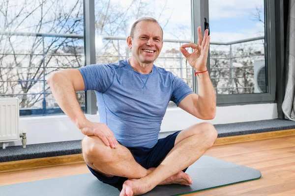 Pozitif sportif orta yaşlı bir adam paspasa oturur ve ışık stüdyosunda sağlıklı bir yaşam tarzı sergiler.