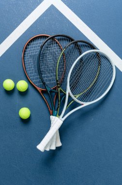 Birden fazla tenis raketi ve beyaz çizgileri olan mavi bir korta yerleştirilmiş yeşil tenis toplarının üst görüntüsü. Spor ekipmanları, eğitim, rekabet ve aktif yaşam tarzı konsepti.