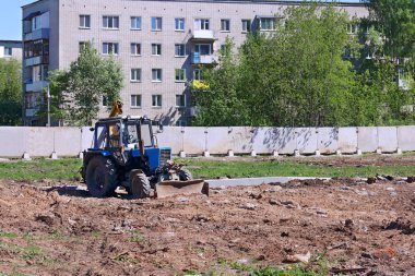 Mavi traktör inşaat çitlerle çevrili sitesi betona çitin yanında çalışıyor.