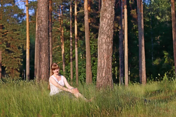 Joven mujer bonita en sonrisas blancas y se sienta en la hierba verde — Foto de Stock