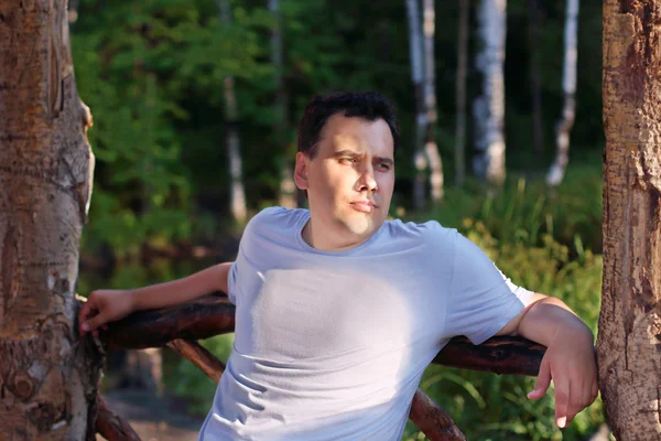 Красивий молодий чоловік сидить в дерев'яній альтанці в літньому парку — стокове фото