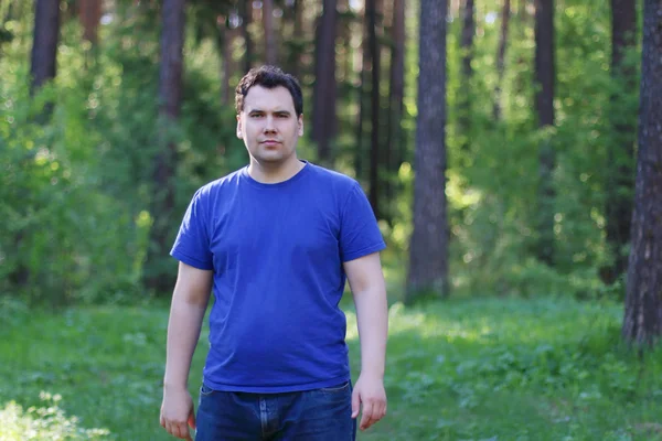 Mooie jonge man in blauw kijkt camera in zomer bos — Stockfoto