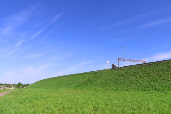 Tiszta kék ég, élénk zöld gyep és a hill road — Stock Fotó