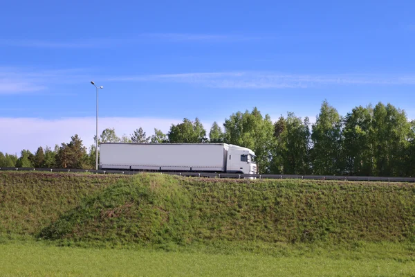 Grande caminhão branco se move na estrada na colina na grama verde — Fotografia de Stock