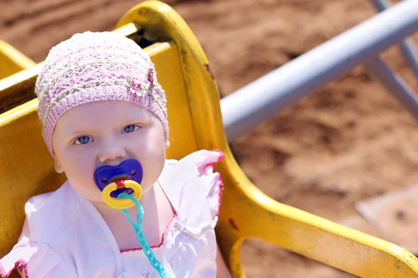 Cute little girl in hat with pacifier riding on carousel — Stock Photo, Image