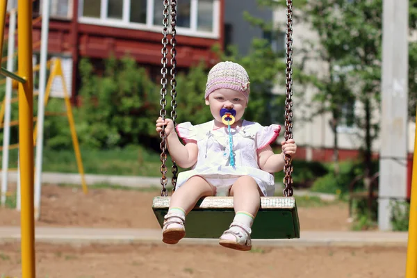 Cute little girl in hat with pacifier riding on swing — Stock Photo, Image