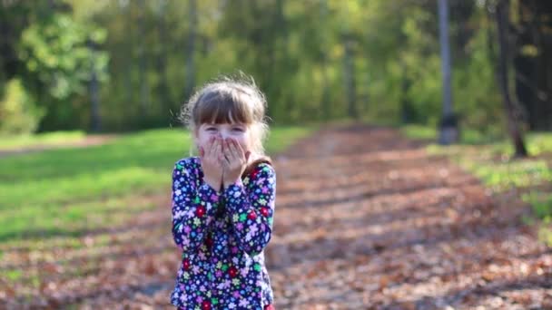 Hermosa niña se ríe y se cubre la boca con las manos en el parque de otoño — Vídeo de stock