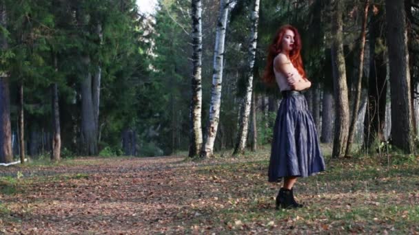 Красивая девушка стоит на сухих листьях в юбке в осеннем лесу — стоковое видео