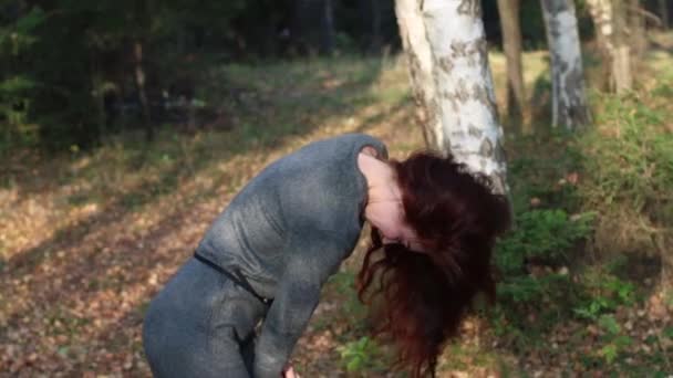 漂亮的女孩，穿着灰色摇摇她的红头发在阳光明媚的森林 — 图库视频影像