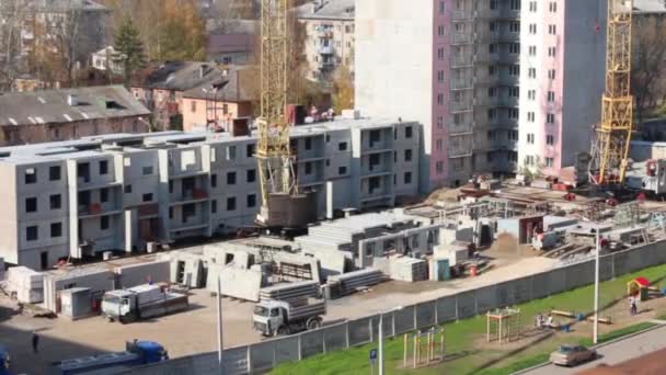 Caminhão se move no local de construção com guindastes e parte do edifício painel de concreto — Vídeo de Stock