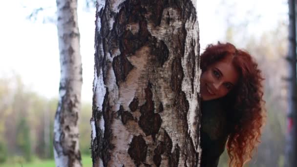 Pretty smiling woman looks out of birch in autumn forest — Stock Video