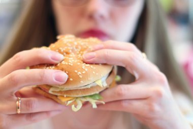 Kadın taze iştah açıcı hamburger kafede yiyor.
