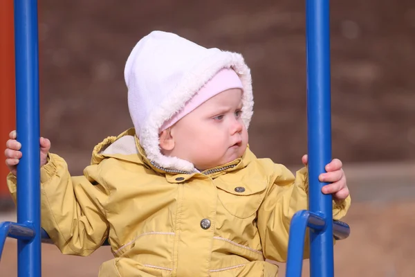 Schattig meisje in gele jas swingt op speelplaats op zonnige — Stockfoto