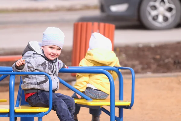 Glad liten pojke och en flicka rida på små carousel på barn pla — Stockfoto