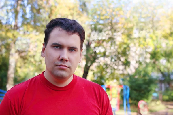 Young handsome man in red stands on children playground at sunny — Stock Photo, Image