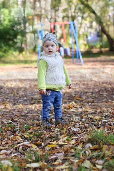 Petite fille mignonne en jeans se tient sur l'aire de jeux au jour d'automne ensoleillé — Photo