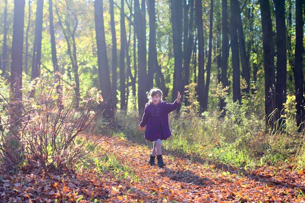 Petite belle fille en manteau court dans le parc parmi les arbres sous le soleil — Photo