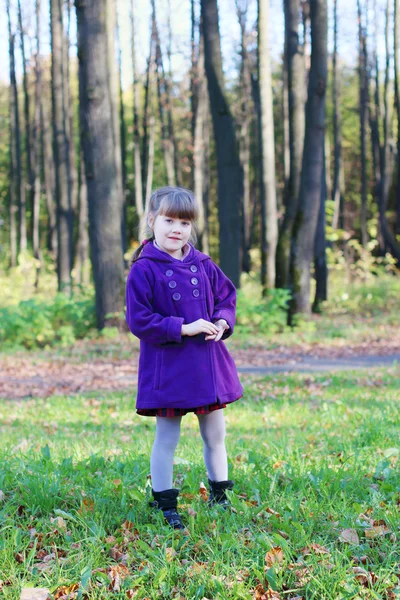 Little beautiful girl in coat stands and looks at camera in sunn — Stock Photo, Image