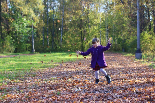 Little beautiful girl in coat throws up leaves in autumn sunny d — Stock Photo, Image