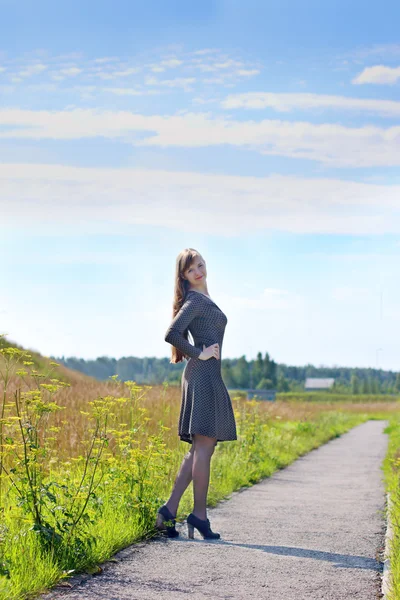 Young cute woman in dress poses on asphalt path at summer sunny — Stock Photo, Image