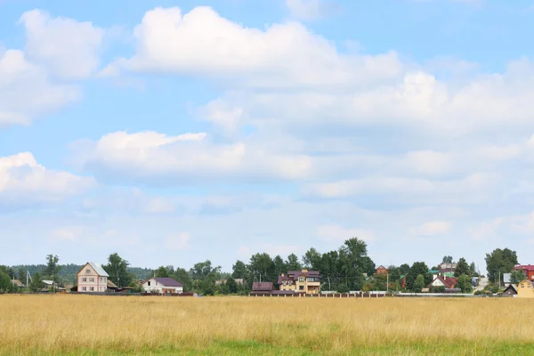 Field with dry grass and houses of village far away at summer su — Stock Photo, Image